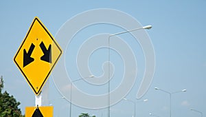 Yellow traffic signs with two white arrow heads indicate the intersection on the road, on blue sky as the background, indicates