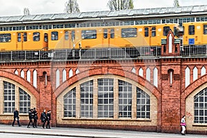 Yellow train on Oberbaum bridge and people walking on the street in city Berlin, Germany