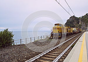 Yellow train parked in front of the ocean in Corniglia, Italy.