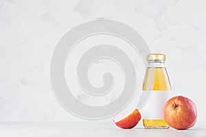 Yellow transperent pear juice in glass bottle mock up with blank label, fruit slice on white wood table in light interior.