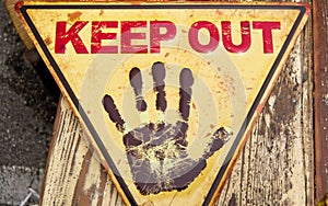 Yellow triangular sign wih keep out in red and an open black hand in stop position