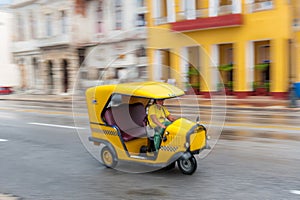 HAVANA, CUBA - OCTOBER 21, 2017: Yellow Tuk Tuk Taxi Vehicle in Havana, Cuba. Woman is Driver