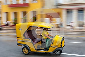 HAVANA, CUBA - OCTOBER 21, 2017: Yellow Tuk Tuk Taxi Vehicle in Havana, Cuba. Woman is Driver