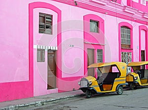 Yellow tuk tuk by pink building Havana, Cuba