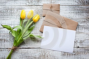 Yellow tulip bouquet and blank greeting card. Top view over wooden table