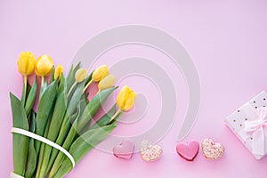 Yellow tulip flowers bouquet and Sweet macaroons in heart shape gift box on pink background.