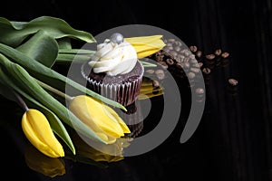 Yellow tulip flowers, homemade cupcake and coffee beans on black background with reflection, sweet cake