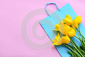 Yellow tulips and blue gift bag on a pink background. Women`s Day concept. Top view, flat lay, copy space