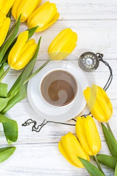 Yellow tulips, a cup of coffee, cappuccino and vintage watch on a chain on a white wooden