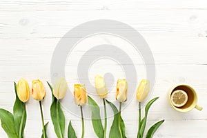 Yellow tulips, cup of tea isolated on a white, wooden background. lay flat, top view