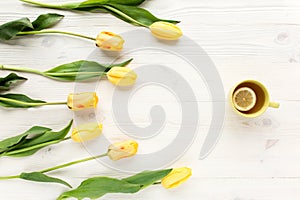 Yellow tulips, cup of tea isolated on a white, wooden background. lay flat, top view