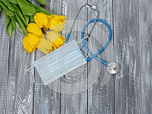 Yellow tulips, kn95 mask and stethoscope on a wooden background. Top view with copy space. Happy Nurse Day. Covid-19