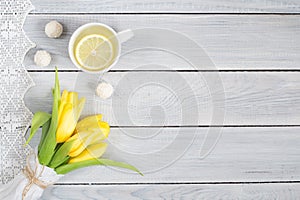 Yellow tulips, lemon tea and candies on white wooden table