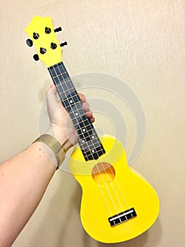 yellow ukulele in a female hand on a beige background. musical instruments