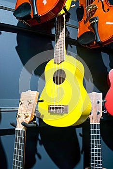 Yellow ukulele and violins hanging on wall sale in music store