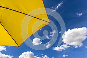 yellow umbrella and blue sky with clouds in the background from behind