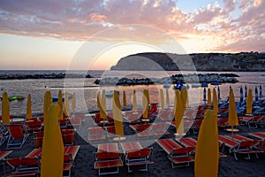 Yellow umbrellas and chaise longue on empty sandy beach at sunset, Ischia, Italy