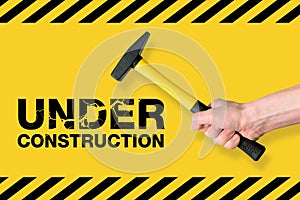 Yellow under construction cracked sign with hammer in human hand