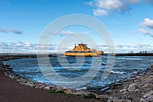 Yellow vehicle ferry rounding a pier outside the port