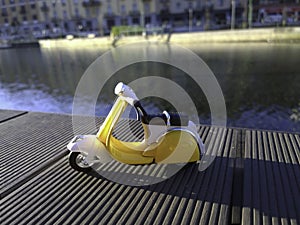 Yellow vespa like model parked in front of the Darsena in Milan Italy