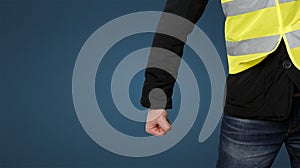 Yellow vests protests. An unrecognizable man clenched his fist in protest on blue background. Concept of revolution and protest