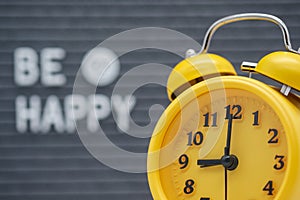 Yellow vintage alarm clock on the background of a gray felt Board with the inscription in English be happy