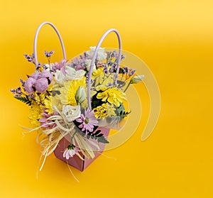 Yellow-violet flower arrangement in a box of chrysanthemums, eustomas, cotton inflorescences and dried flowers on a yellow