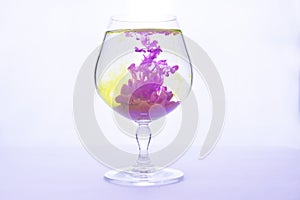 Yellow and violet paints fall in a wineglass with water