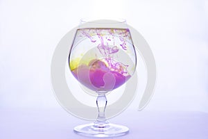 Yellow and violet paints fall in a wineglass with water