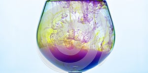 Yellow and violet paints fall in a wineglass with water