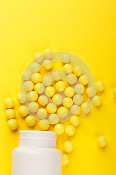 Yellow vitamin C capsules spilled out of a white jar against a Yellow background. Take care of your health. Vitamins and