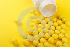 Yellow vitamin C capsules spilled out of a white jar against a Yellow background. Take care of your health. Vitamins and