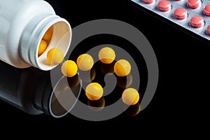 Yellow vitamins are sprinkled from a white bottle and pills on a black isolated background. Free advertising space