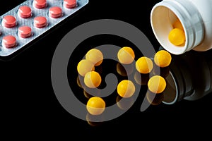 Yellow vitamins are sprinkled from a white bottle and pills on a black isolated background. Free advertising space