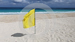 Yellow warning flag indicating adverse conditions or dangerous rip currents on a tropical white sand beach