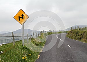 Yellow warning sign of a curvy road under a cloudy sky