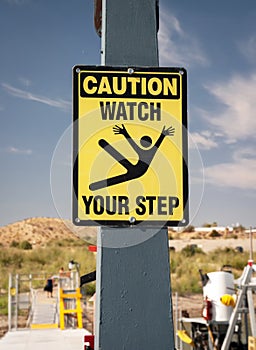 Yellow watch your step sign with graphic of a person falling at a boat dock