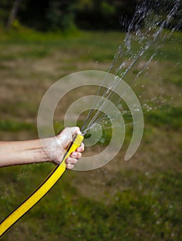 Yellow watering hose with jet of water in the hand of teenager watering the lawn