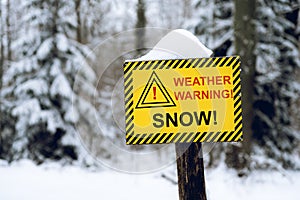 Yellow weather warning snow sign in the out of focus forest background