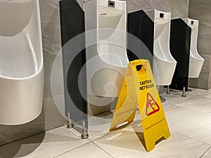 Yellow wet floor caution sign after cleaning in public male toilet