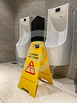 Yellow wet floor caution sign in public male toilet room