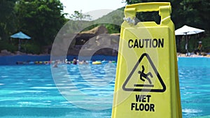 Yellow wet floor caution sign on swimming pool background in amusement water park. Caution wet floor sign in aqua park