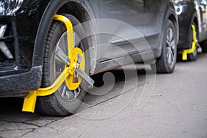 Yellow wheel lock on a random car in the street. Traffic parking violation, common punishment for blocking a car from moving