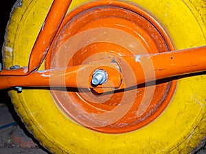 A yellow wheel with an orange disc of a garden wheelbarrow