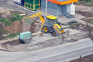 Yellow wheeled excavator digs a trench in the city