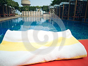 Yellow and white coloured towel on the poolside of a calm beautiful swimming pool