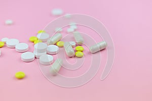 Yellow and white pills and capsules on a pink background. Medical background.