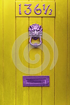 Yellow wooden door with purple door knock and mailbox