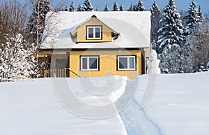 Yellow wooden house and snowman on forest background in winter sunny day