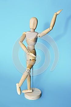 Yellow wooden maniken is dancing and doing poses on blue background